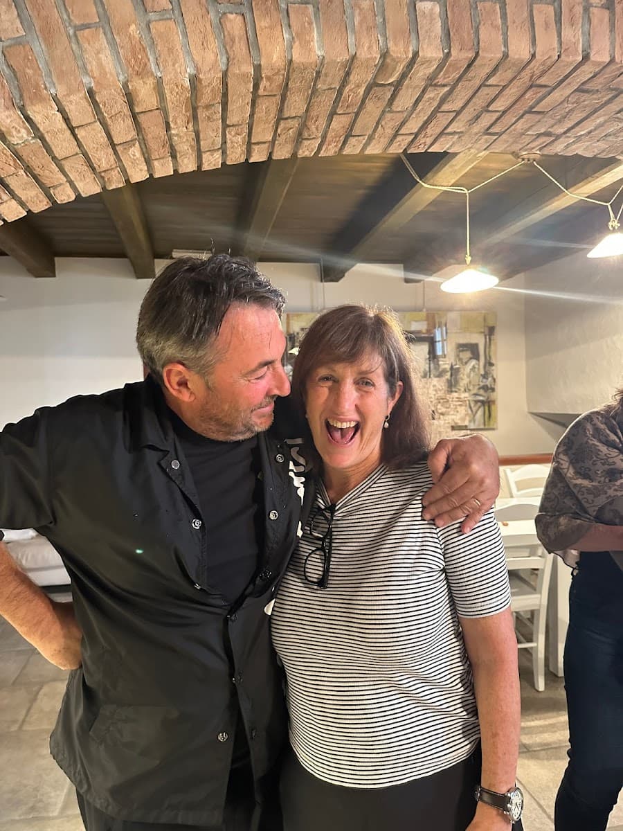 Two people smiling indoors under a brick archway with hanging pendant lights