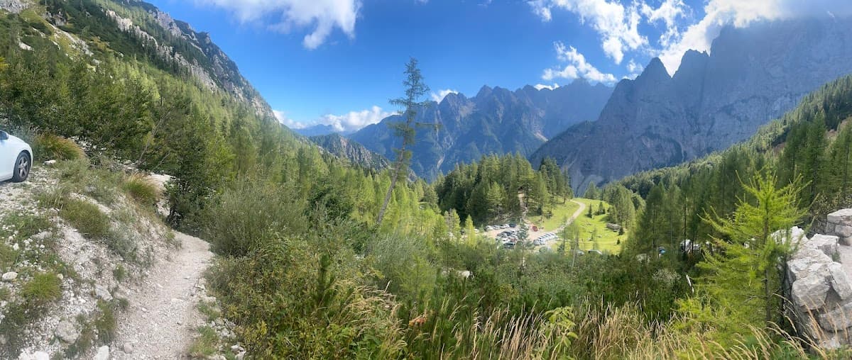 Mountain valley landscape with pine forest, parking lot, and rugged peaks under blue sky