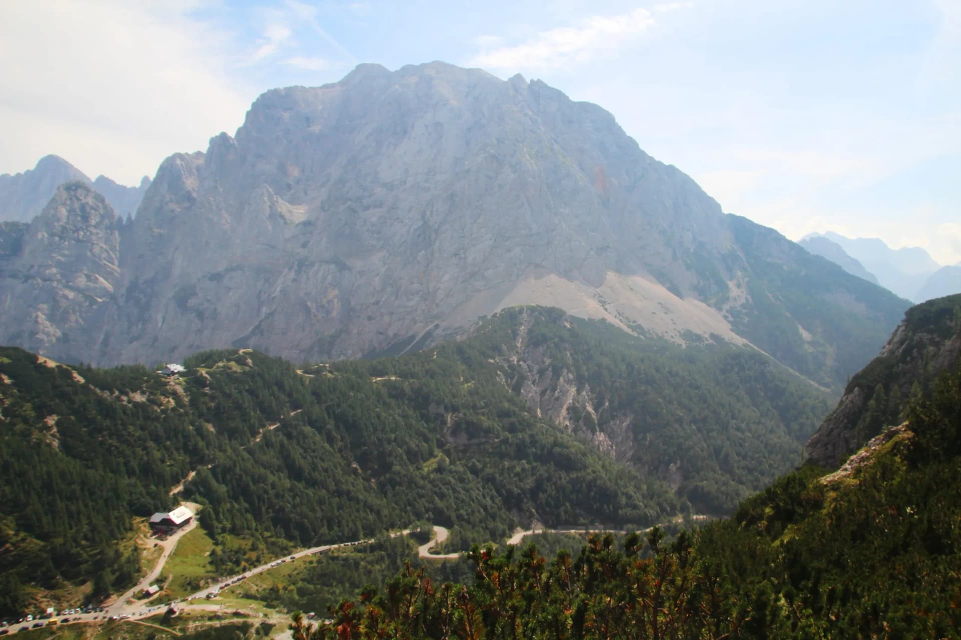 Winding mountain road below massive rocky peaks and green forested slopes at Vršič Pass, Slovenia.