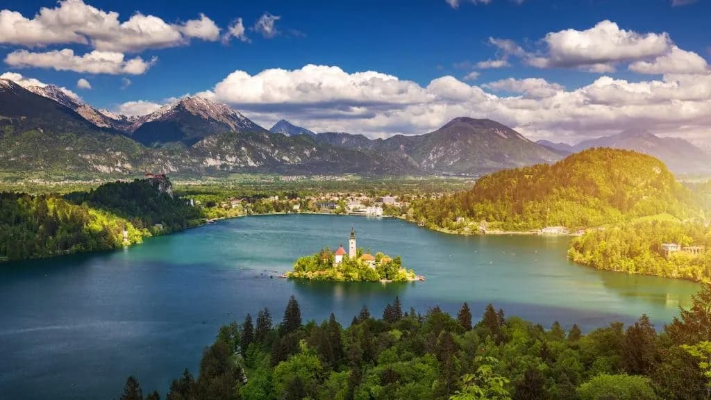 Panoramic view of Lake Bled island church with Julian Alps under blue sky and clouds