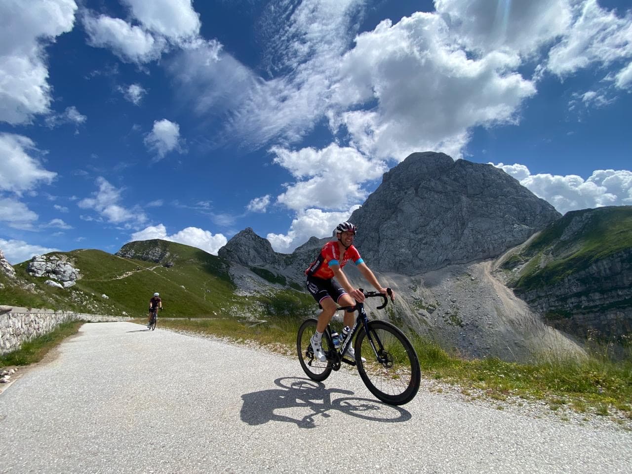 Cyclists riding on paved mountain road with large rocky peaks under blue sky