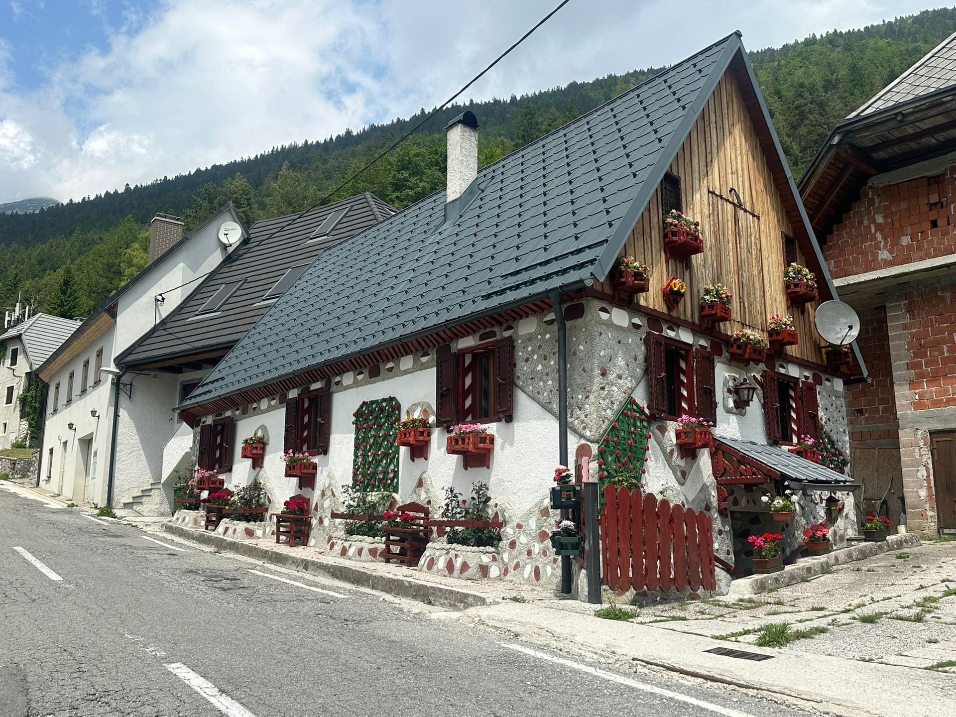 Traditional Slovenian house in Strmec village with stone facade and flower boxes against forested mountains.