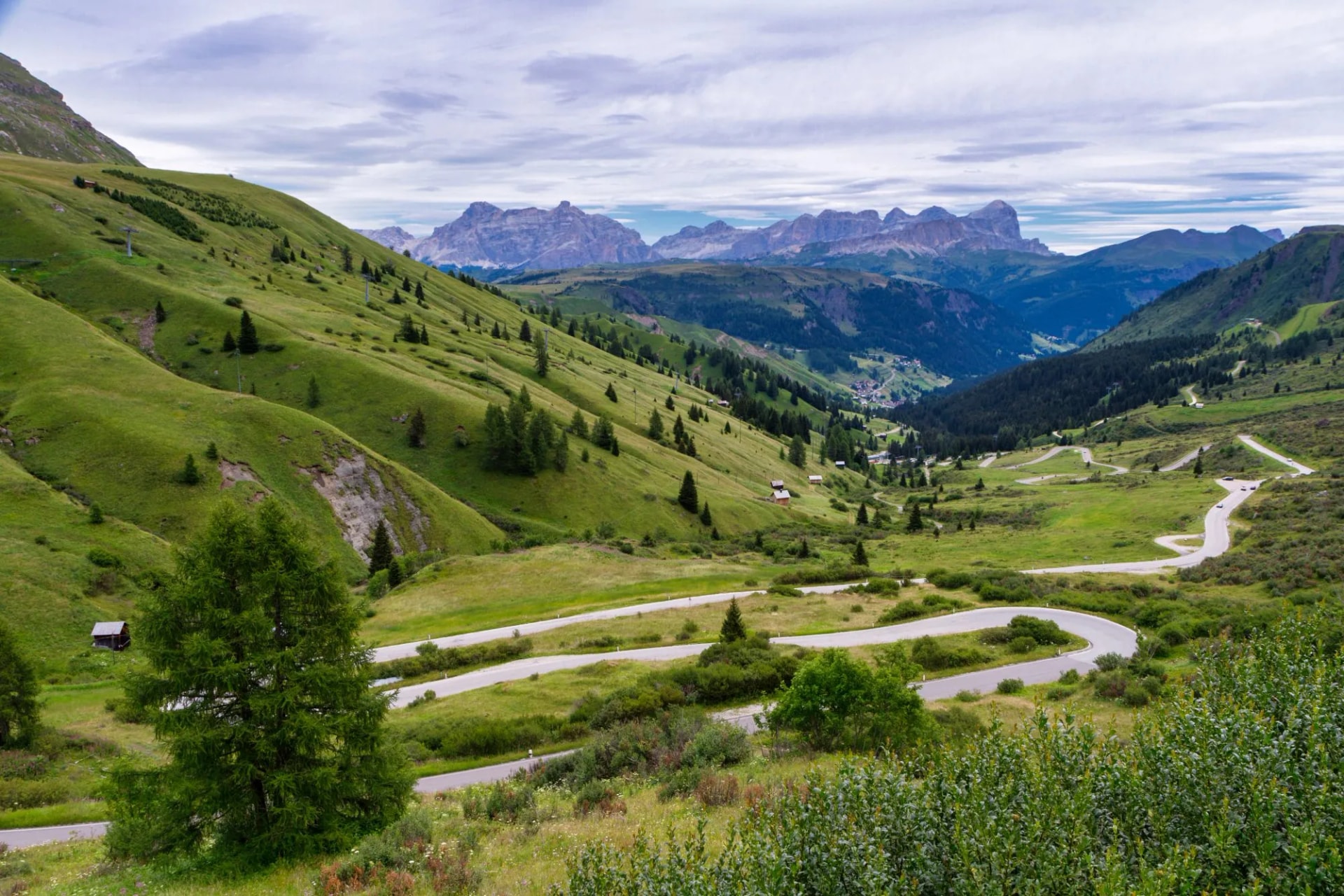 Winding mountain road at Pordoi Pass with green slopes and distant Dolomites peaks