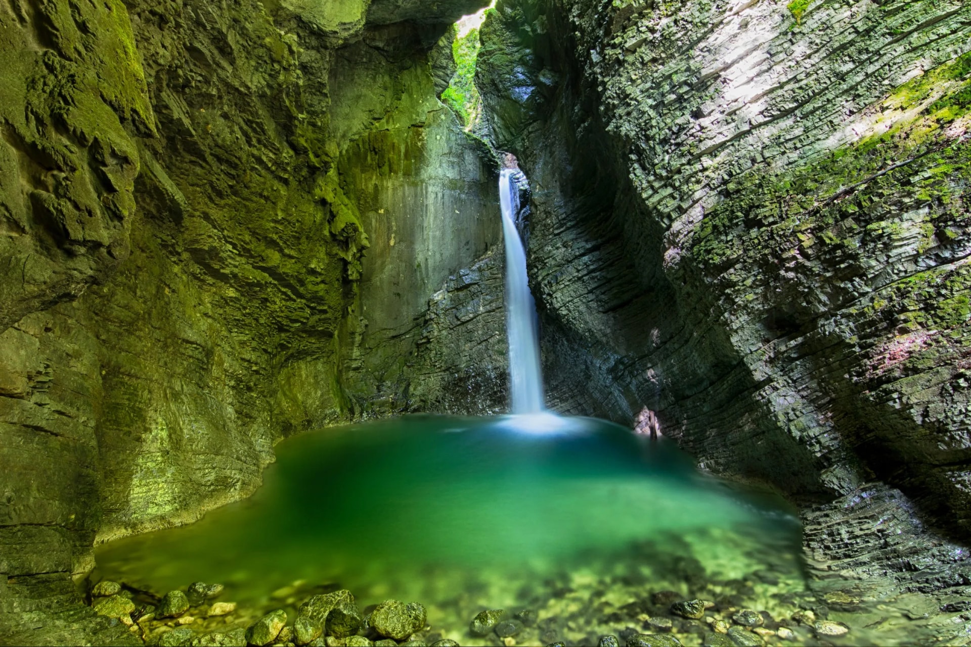 Waterfall cascading into a green pool inside a mossy, narrow rock gorge, Kozjak.