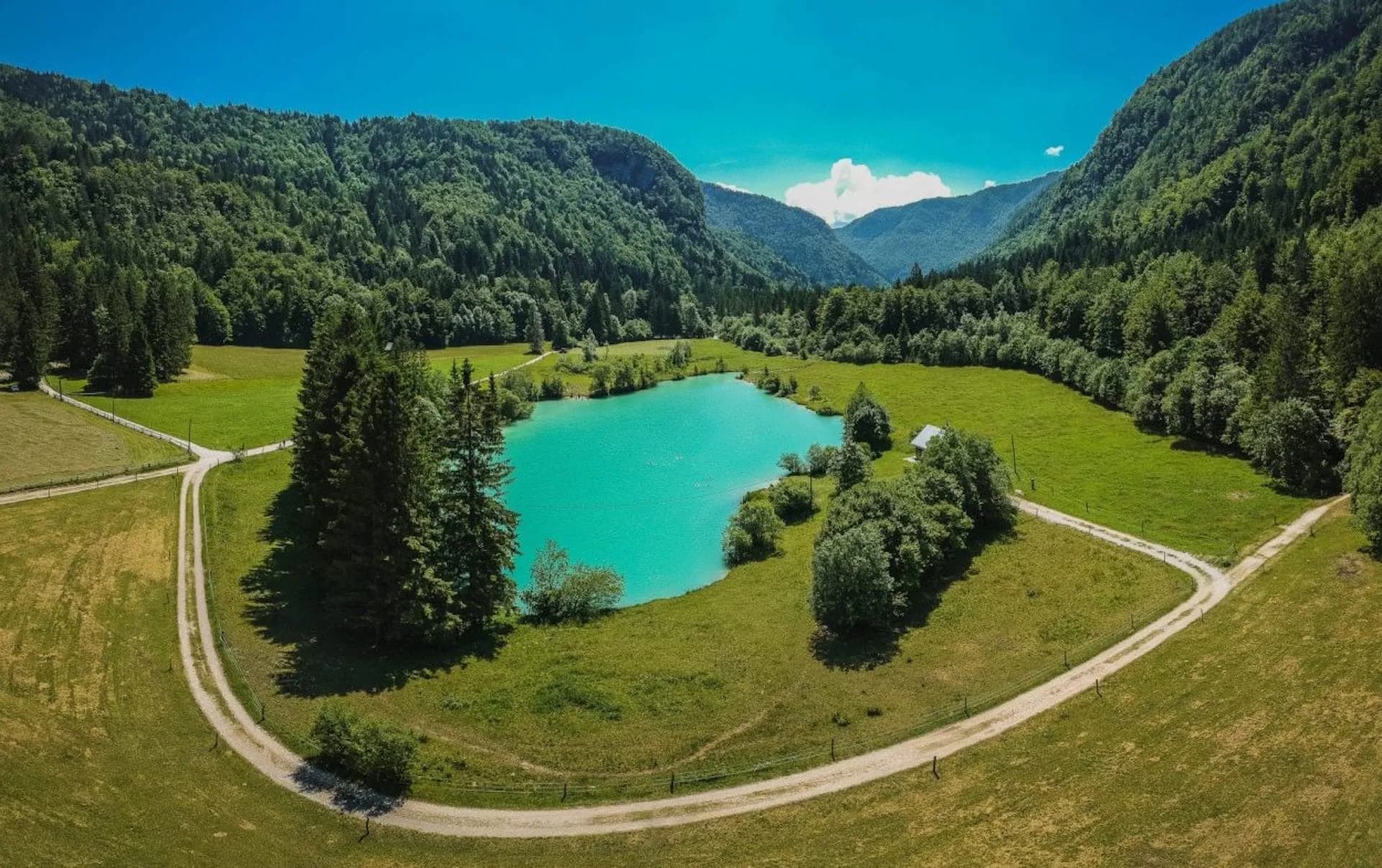Radovna Valley with bright turquoise Kreda lake surrounded by green forested mountains under a blue sky.