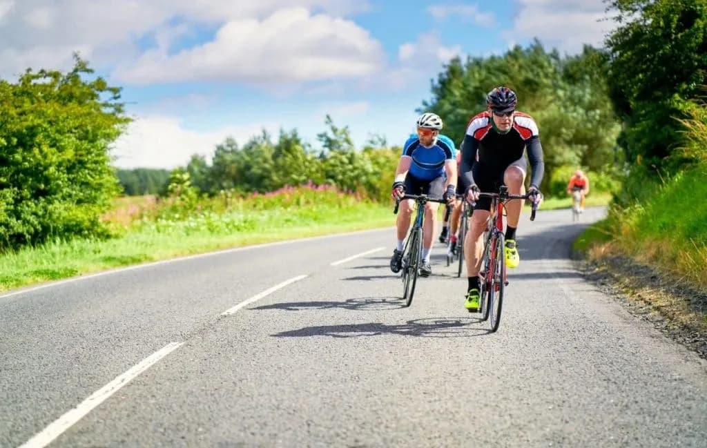 Group of road cyclists riding on an asphalt road through green countryside under a blue sky.