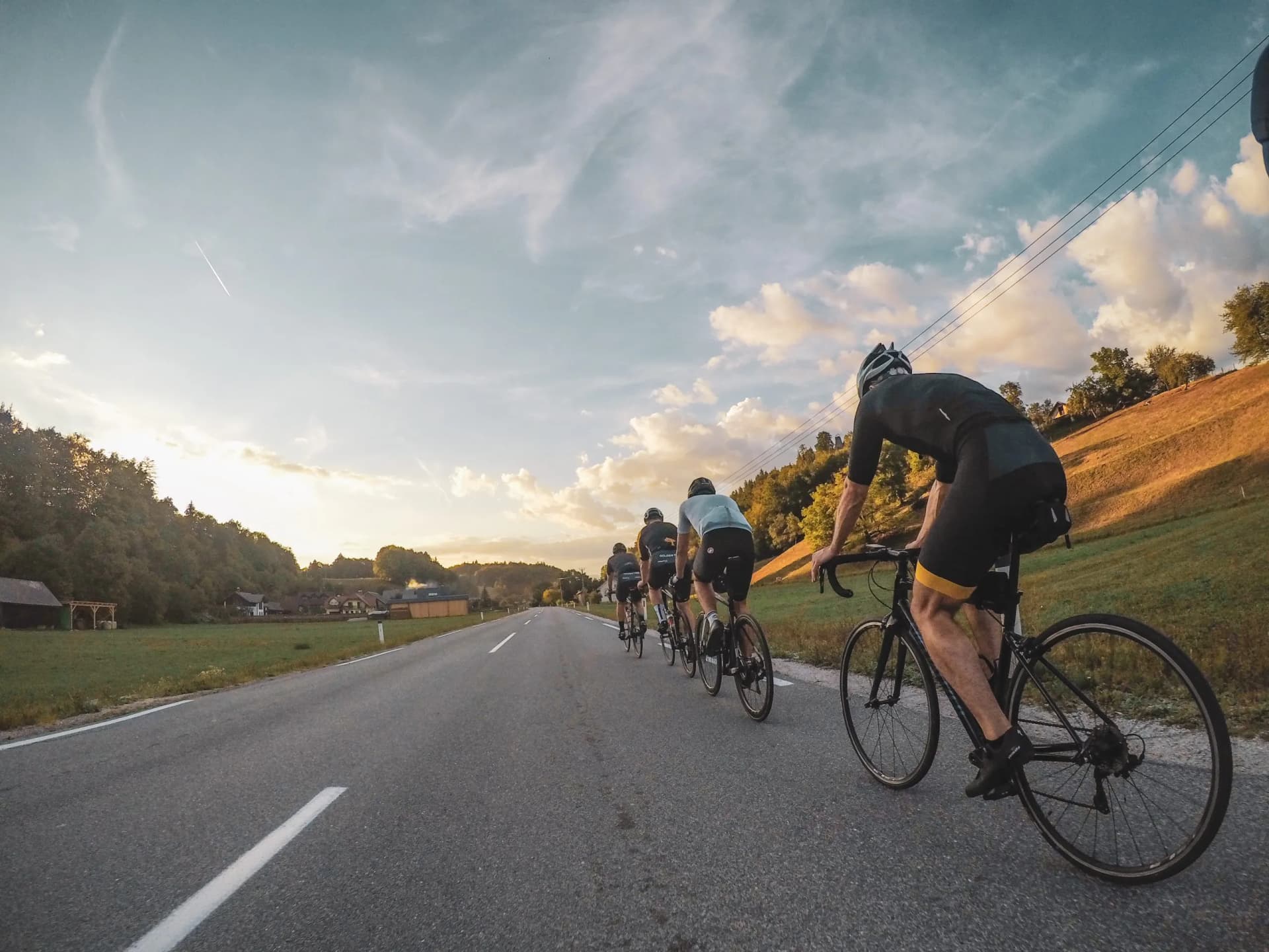 Group cycling on paved road through rolling hills near sunset in a rural area.