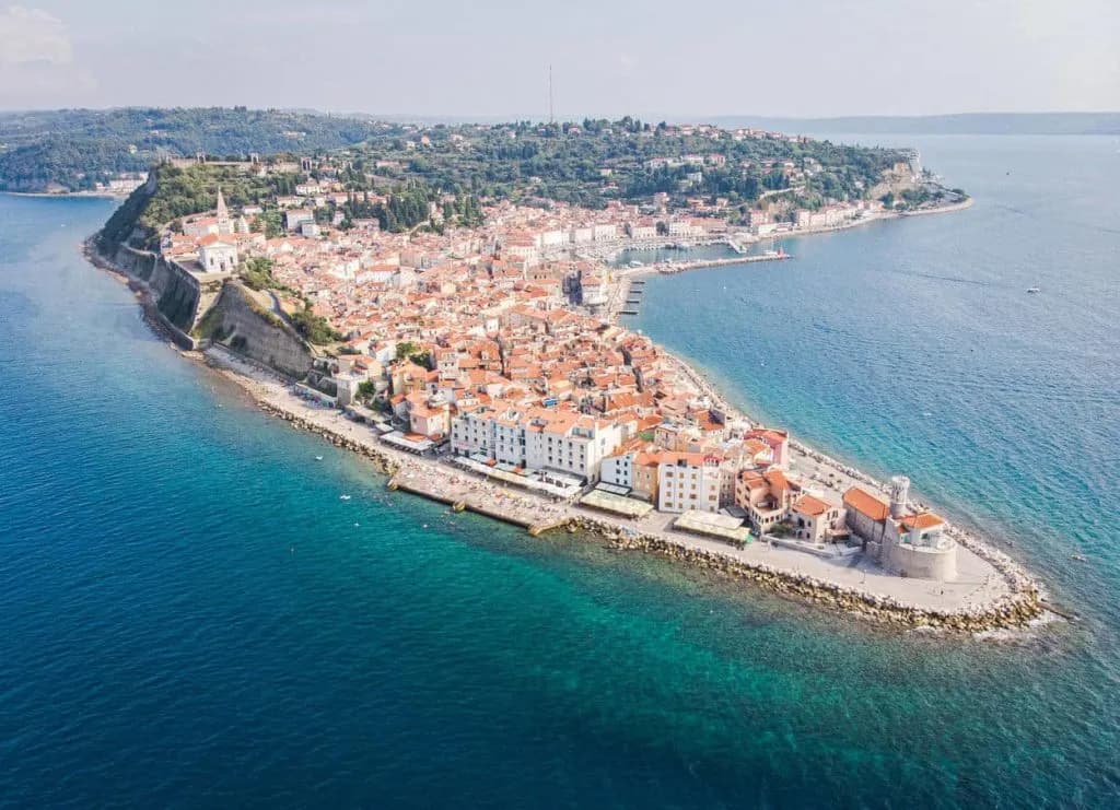 Aerial view of Piran peninsula, Slovenia, with terracotta roofs and clear blue Adriatic Sea.