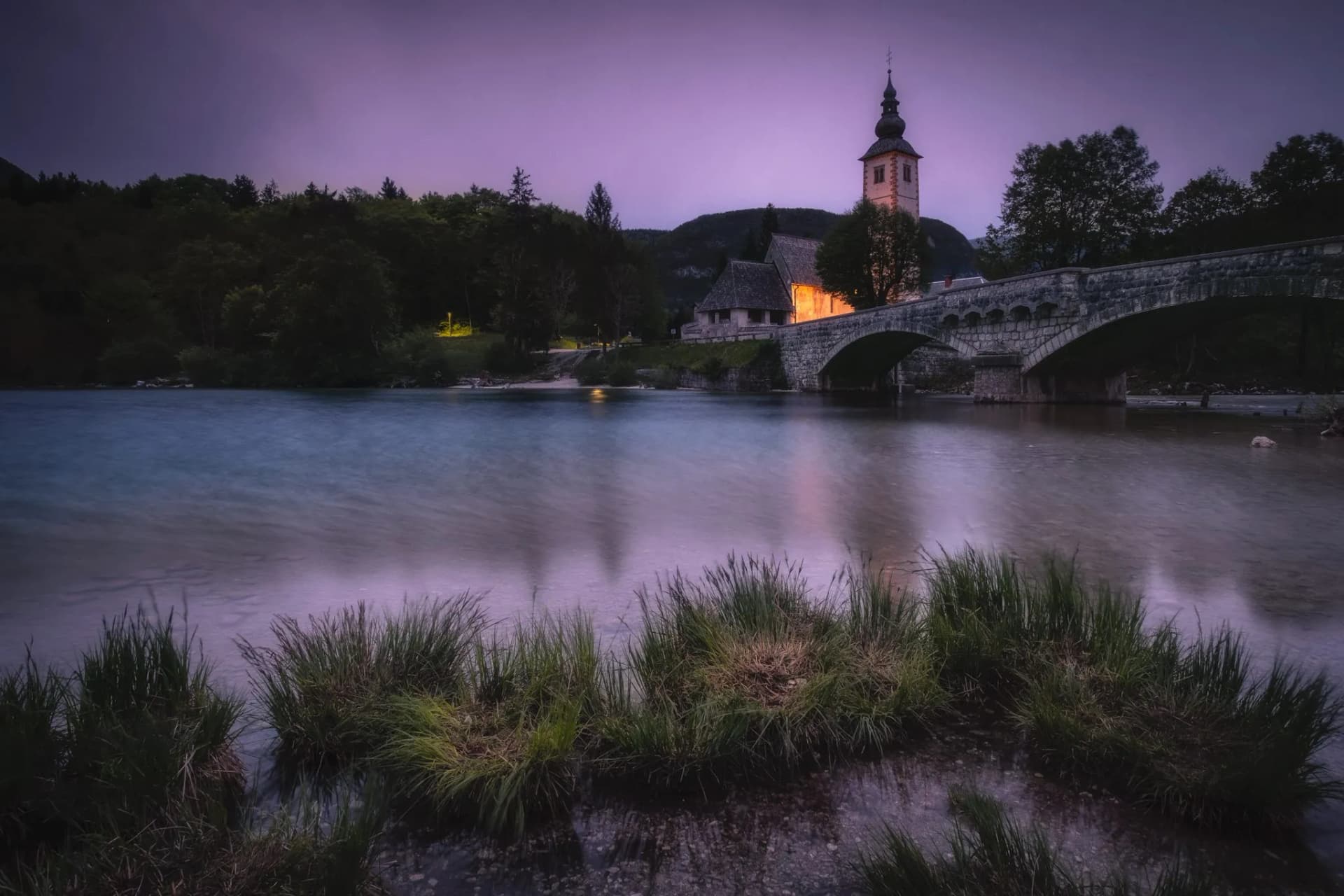 Church tower and stone bridge over river at dusk near Bohinj Lake, Slovenia