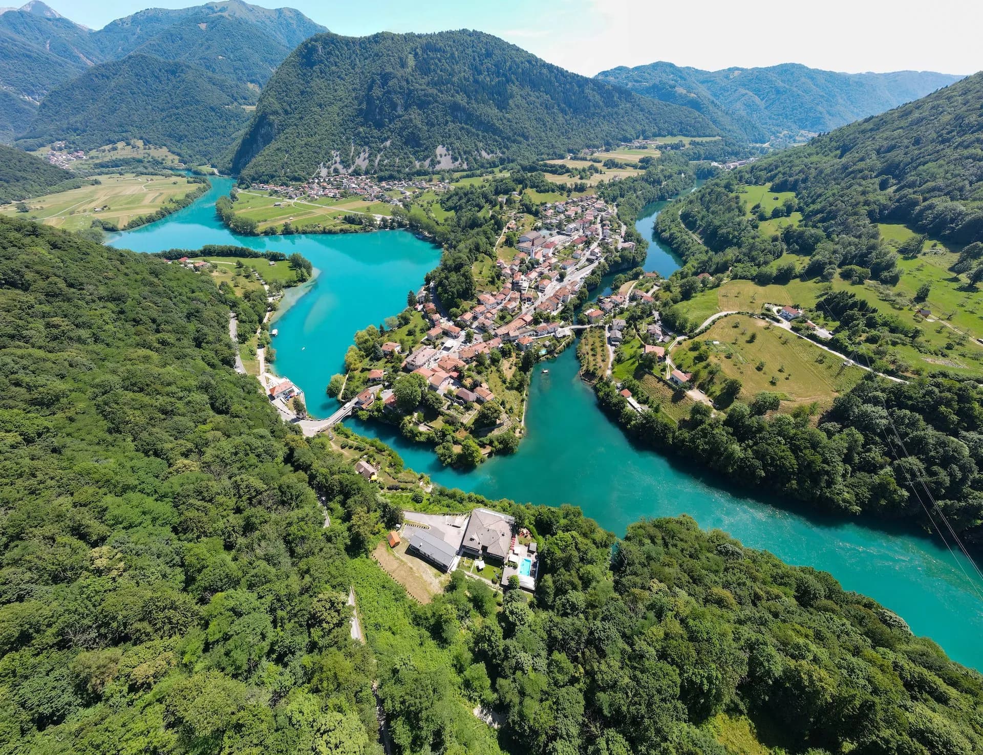 Aerial view of a town nestled between turquoise river bends surrounded by lush green mountains.