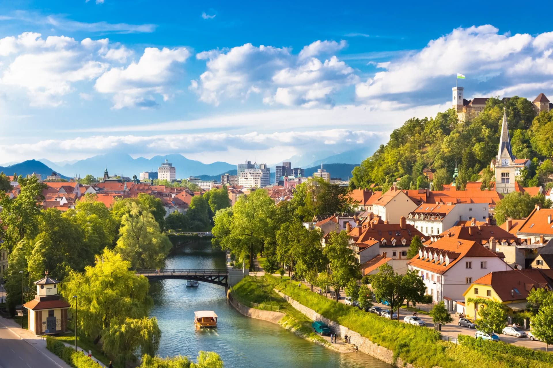 Ljubljana cityscape with riverboats, Ljubljana Castle, and Julian Alps in the background