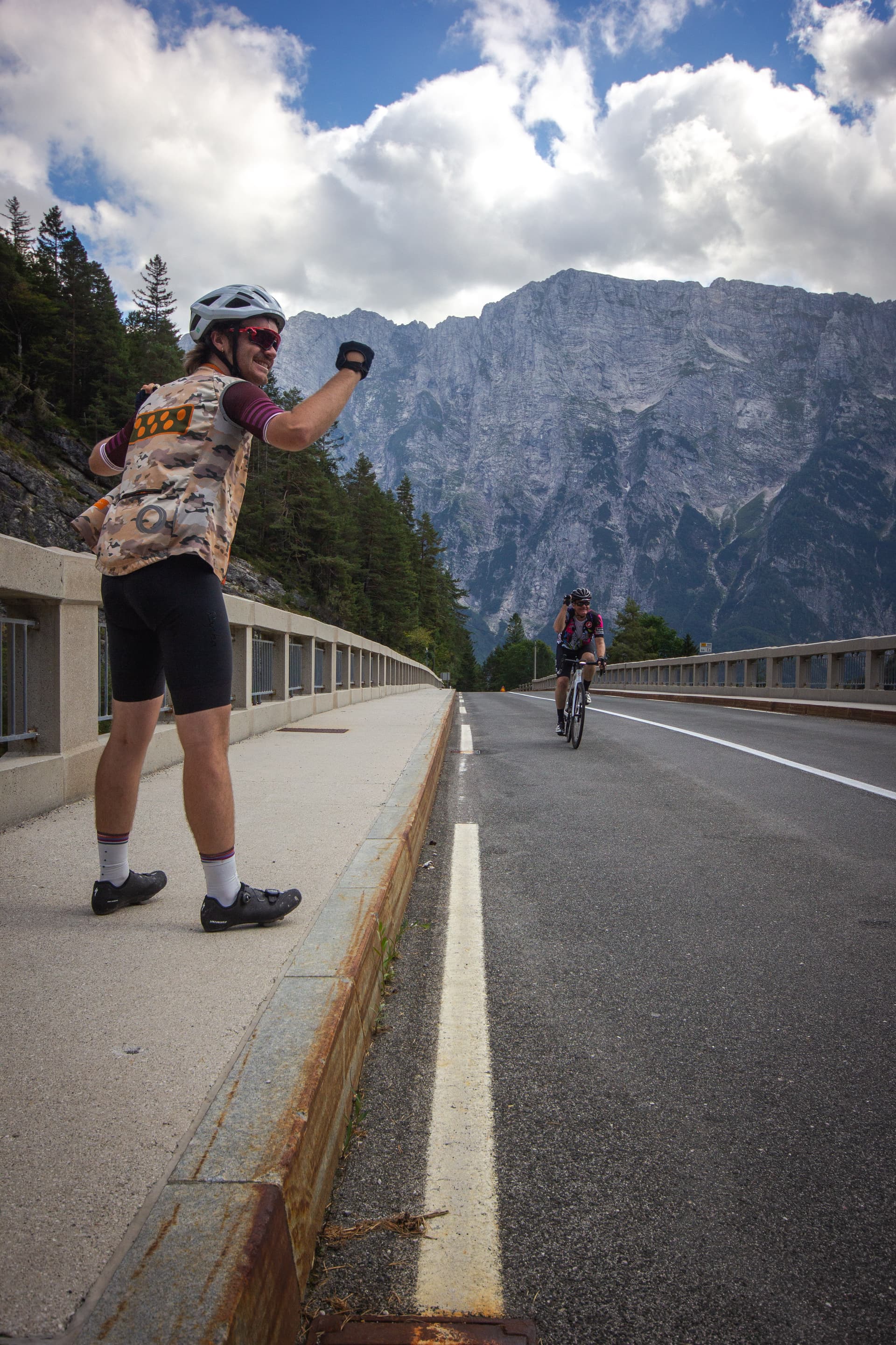 Cyclists on bridge with massive rocky mountain backdrop under cloudy sky in Slovenia