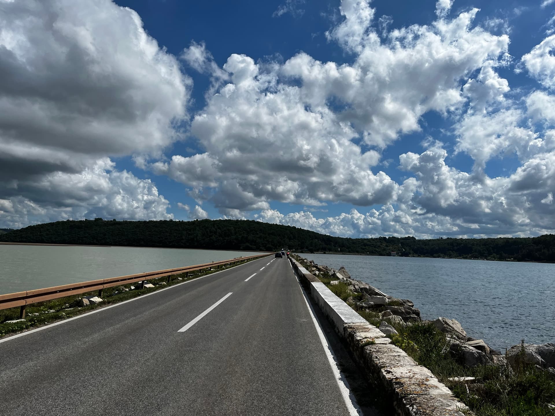 Road across a dam separating two bodies of water under a cloudy sky